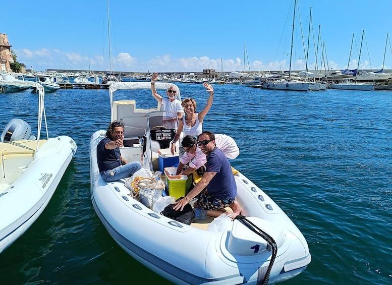 A group of people on a small inflatable boat in a marina with multiple sailboats docked in the background. 4