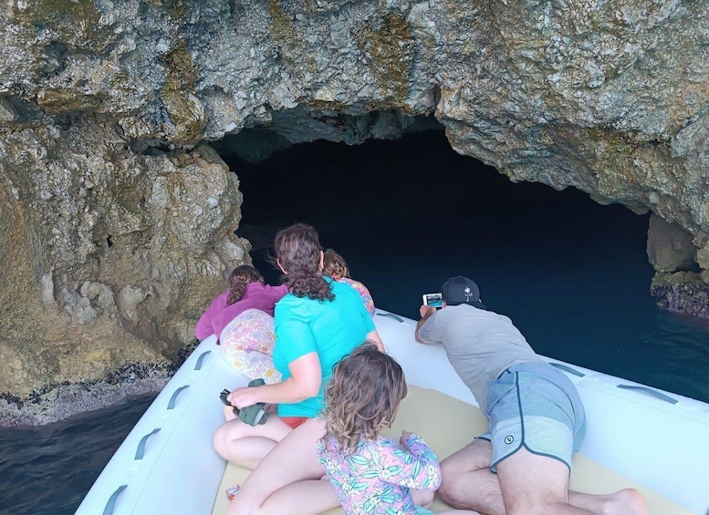 A group of people on a boat near a rocky cave entrance. 2