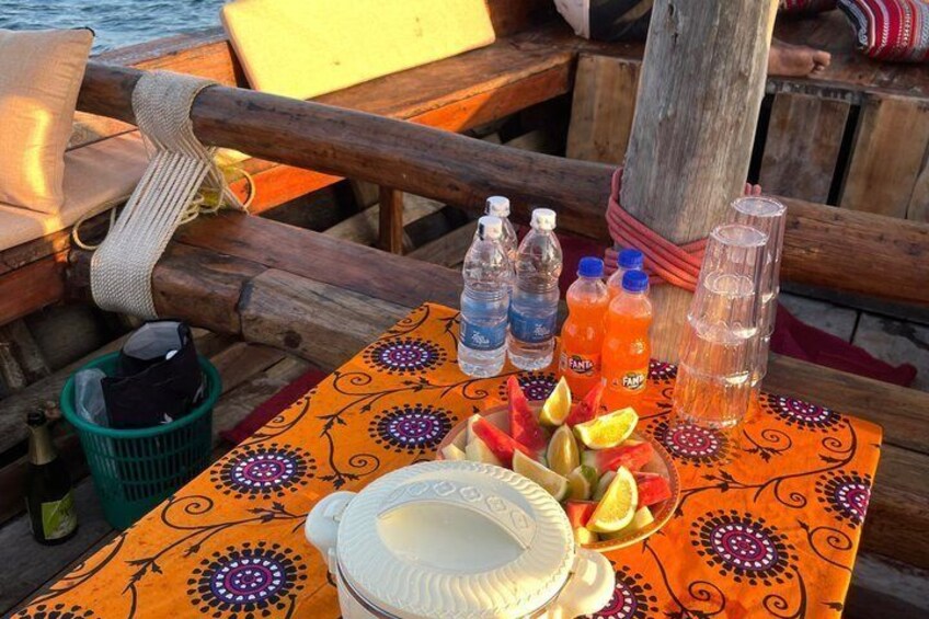 A table with a patterned tablecloth, plates, glasses, and bottles of water and juice on a boat. 2