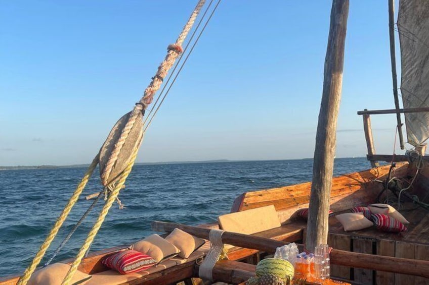 A wooden boat with ropes and cushions on deck, sailing on calm waters. 1
