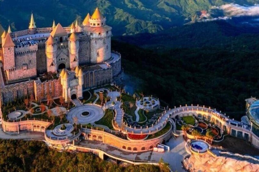 A castle with multiple towers, a winding pathway, and a mountainous backdrop. 1