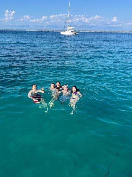 A group of people swimming in clear blue water with a sailboat in the distance. 3