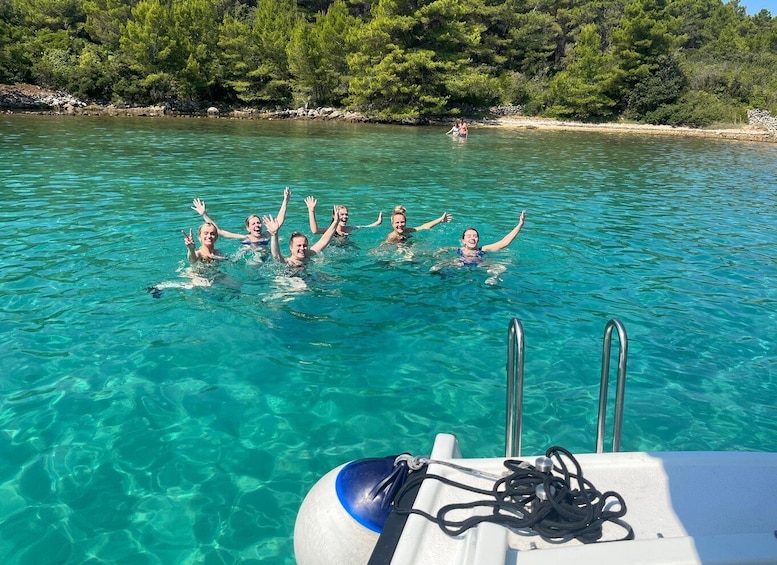 A group of people swimming in clear turquoise water, with a boat and rocky shoreline in the background. 2