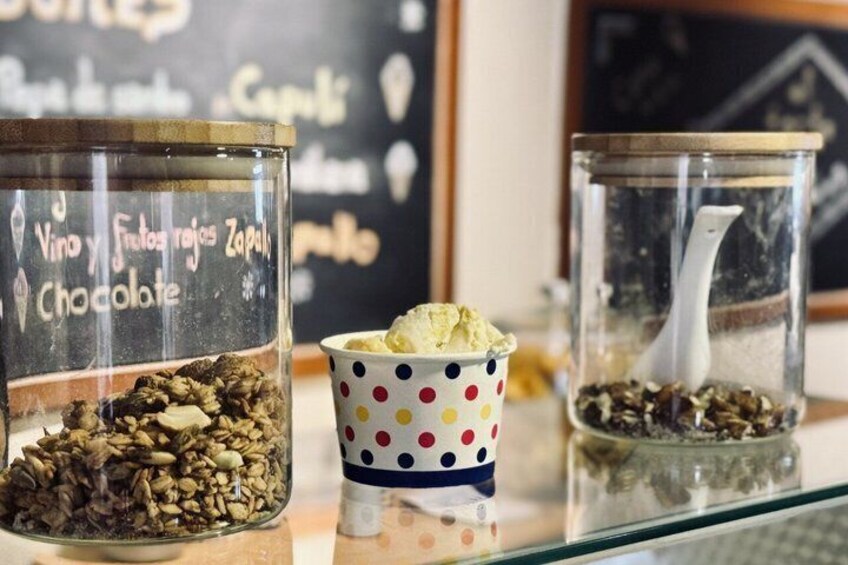 Three glass jars with labels, one containing chocolate and another with seeds, and a polka-dotted cup in between. 2