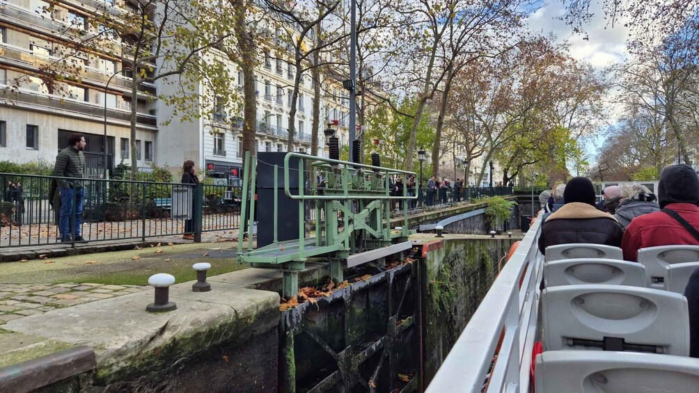 A green metal bridge over a canal with people on it, surrounded by trees and buildings. 2