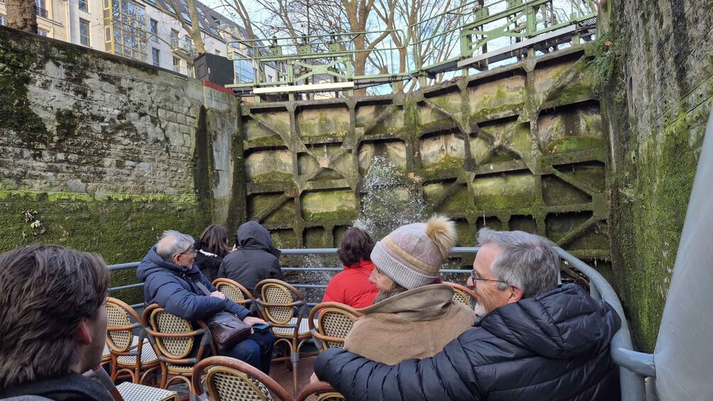 People seated on wicker chairs facing a large, moss-covered metal structure. 3