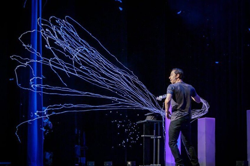 A person standing on a stage with a microphone, surrounded by blue light effects. 2
