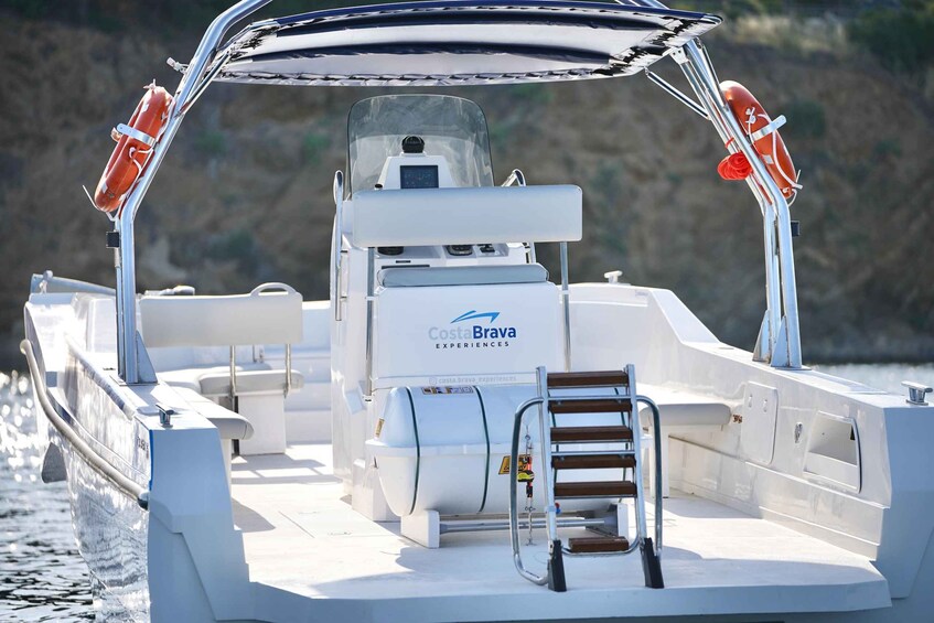 A boat with a CostaBrava Experiences logo, life preservers, a steering wheel, and a wooden bench. 2