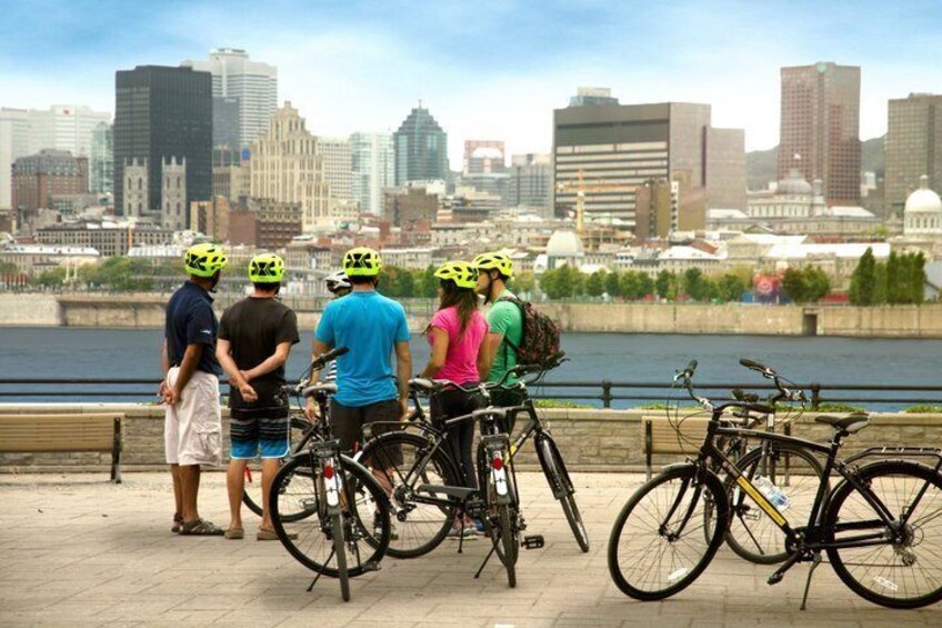A group of people with bicycles by a waterfront with a city skyline in the background. 4