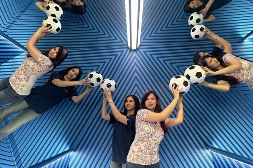 A group of people lying on the floor, holding soccer balls in a patterned room. 1