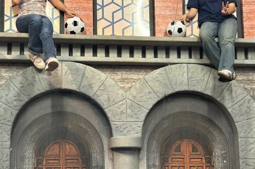 Two people sitting on a ledge with soccer balls, a stone archway, and a wooden door. 4