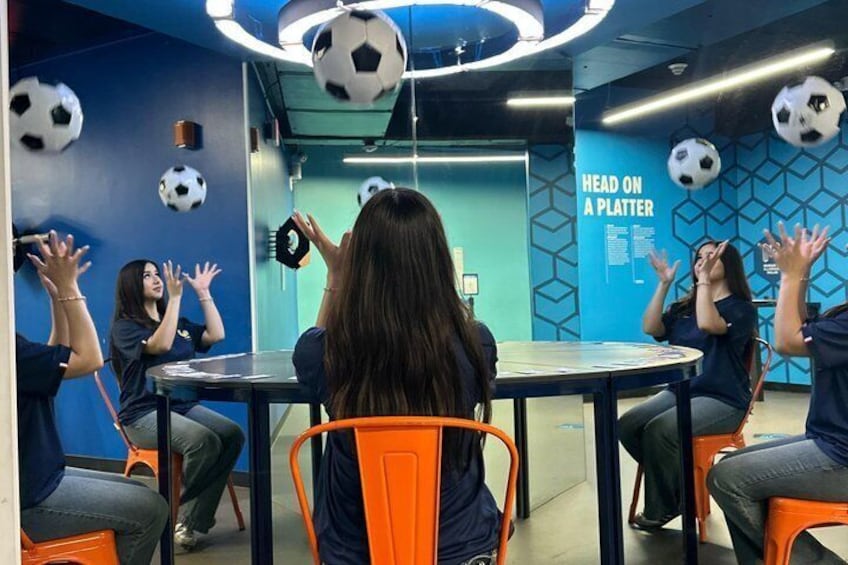 A group of people sitting around a table in a room with blue walls and soccer balls hanging from the ceiling. 2