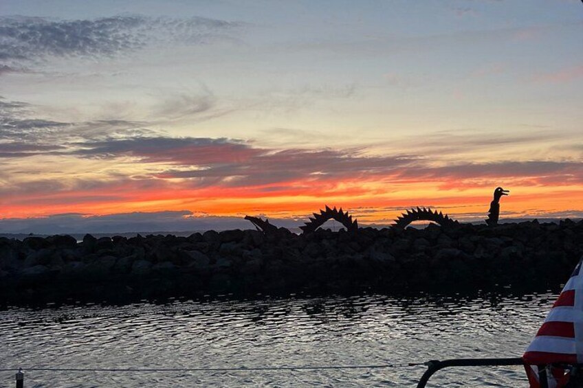 A sunset over a rocky shoreline with a sculpture of a bird. 3