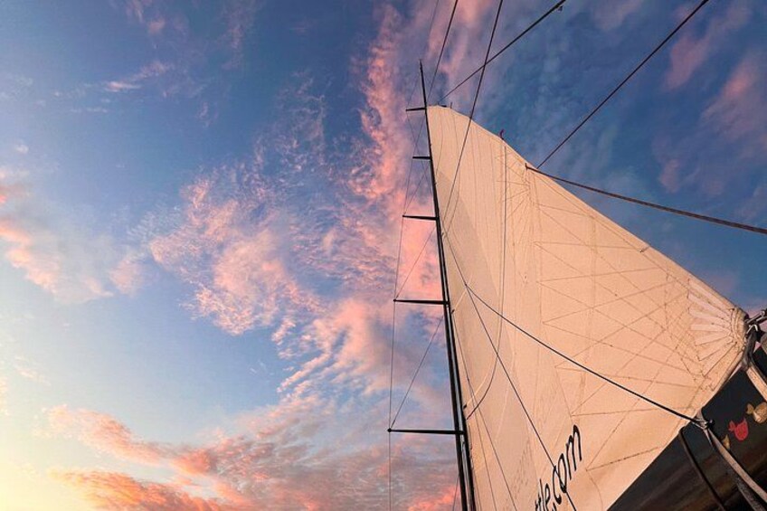 A sailboat with a white sail against a sky with pink and blue clouds. 2