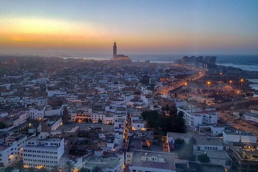 A coastal cityscape at dusk with a prominent tower in the distance, dense urban development, and a coastline. 5