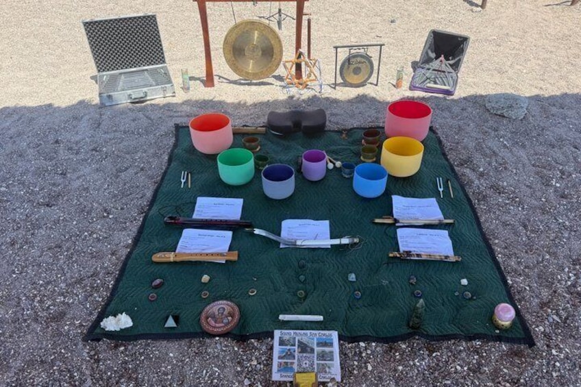 A table with colorful bowls, sticks, and papers on a green mat outdoors. 3