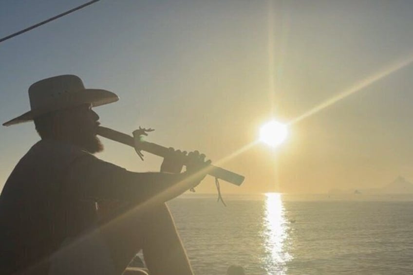 A person playing a guitar on a boat with the sun setting in the background. 2