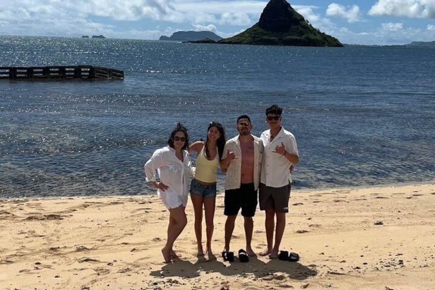 A group of people on a sandy beach with a body of water and a small island in the distance. 4