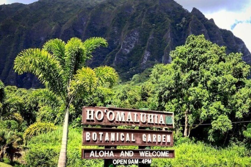 A sign for Ho'Omaluahia Botanical Garden with a mountainous backdrop. 3