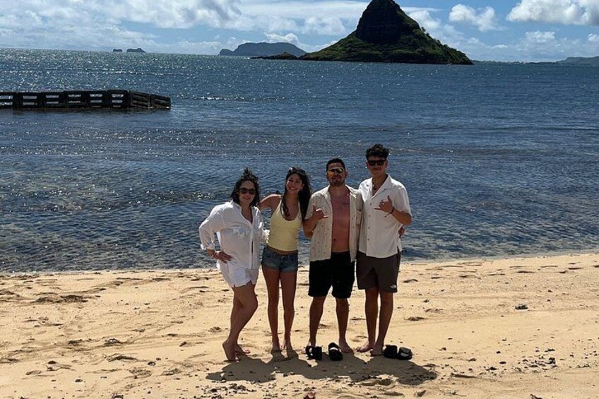 Ein Strand mit vier Personen, einer Holzstege und einem Berg im Hintergrund. 4