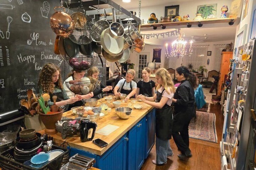 A group of people cooking in a kitchen with pots hanging above the counter. 1