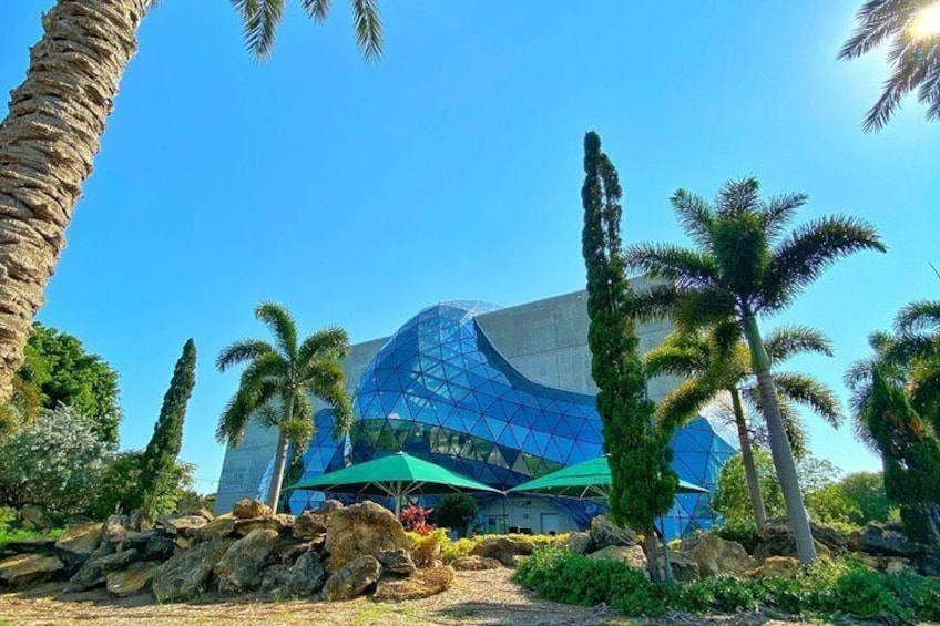 A modern building with a glass facade, surrounded by palm trees and rocks. 3