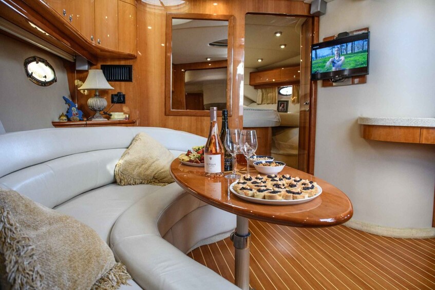 A yacht interior with a curved sofa, a wooden table with food and drinks, a TV, and a mirror. 2