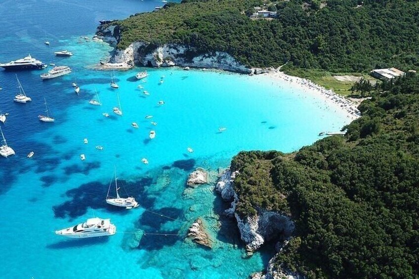 A coastal area with clear turquoise waters, numerous boats, rocky outcrops, and lush greenery. 2