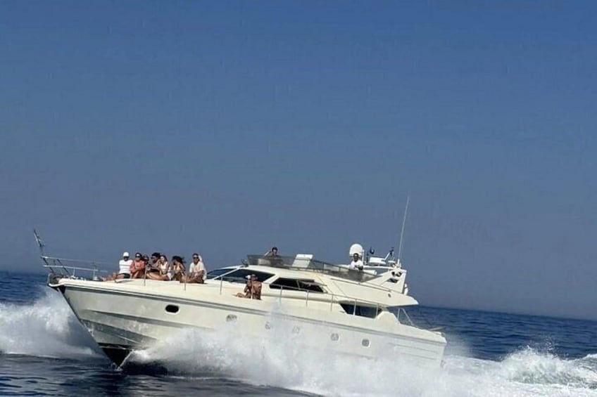 A white yacht with passengers on deck, moving through the water. 3