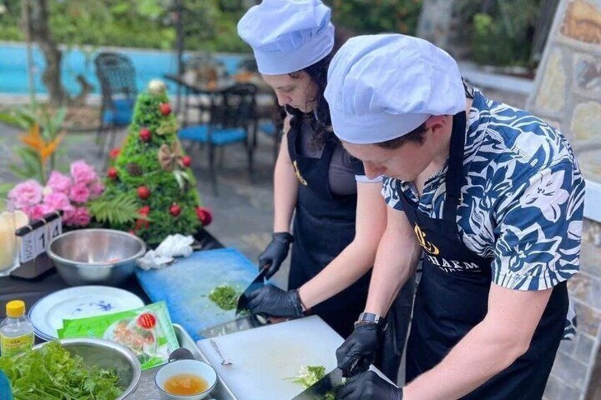 Two people preparing food outdoors with a table full of ingredients and a Christmas tree in the background. 5