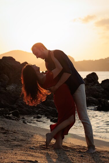 A couple embracing on a beach with rocks and water in the background. 4