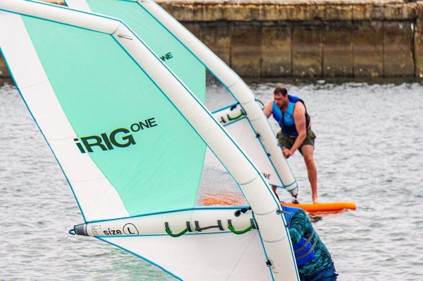 A person windsurfing with a sail labeled 'iRig One' on a body of water. 2