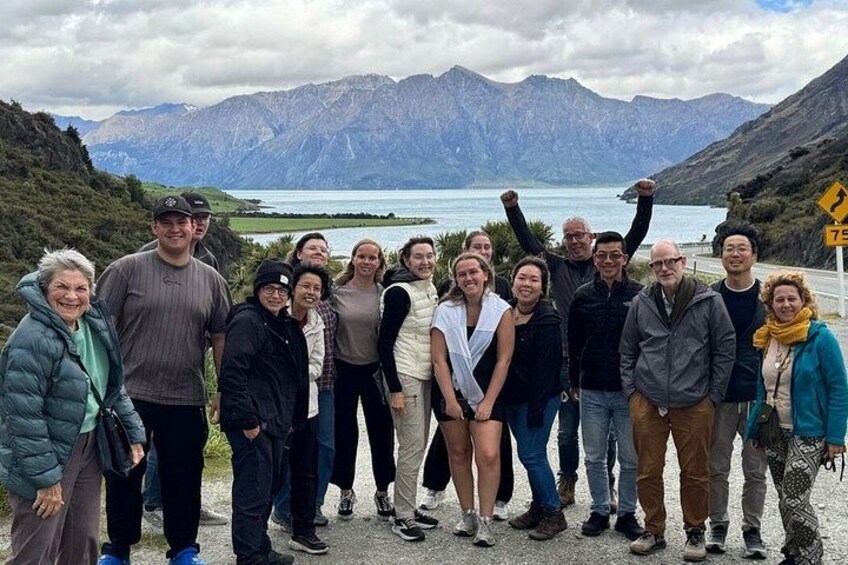 A group of people standing on a path with a mountainous landscape and a lake in the background. 3