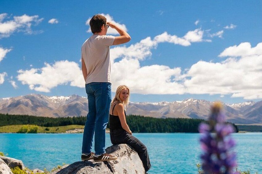 A man and a woman on a rocky outcrop overlooking a lake with mountains in the background. 1