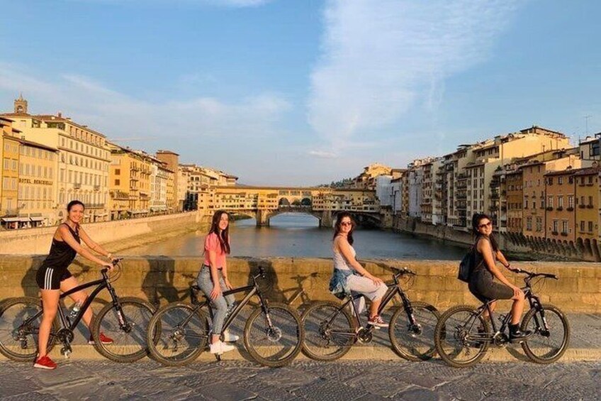 A group of people on bicycles along a riverside walkway with historic buildings in the background. 2