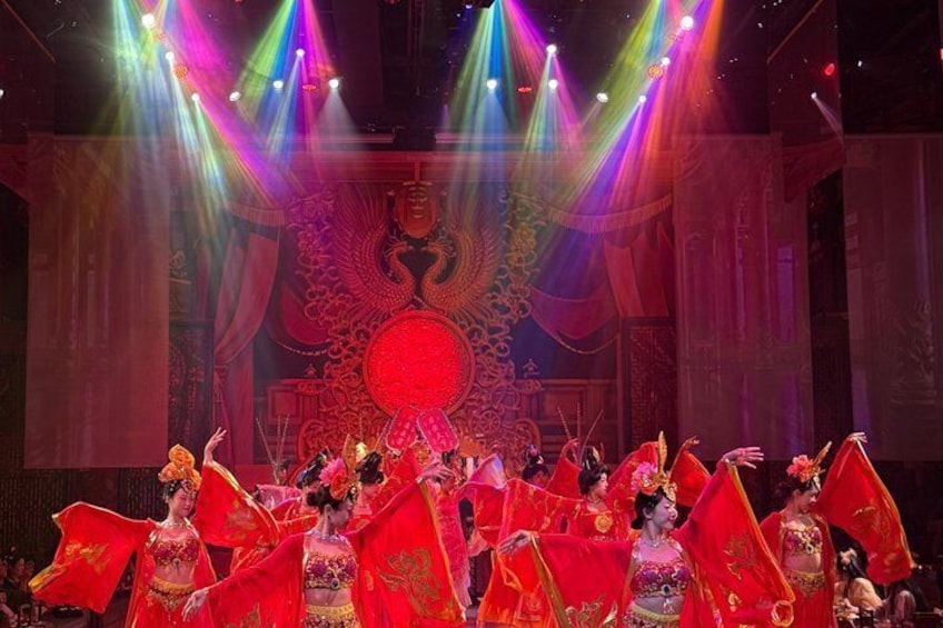 A traditional dance performance with performers in red costumes and fans, set against a backdrop with a large circular emblem and ornate patterns. 4