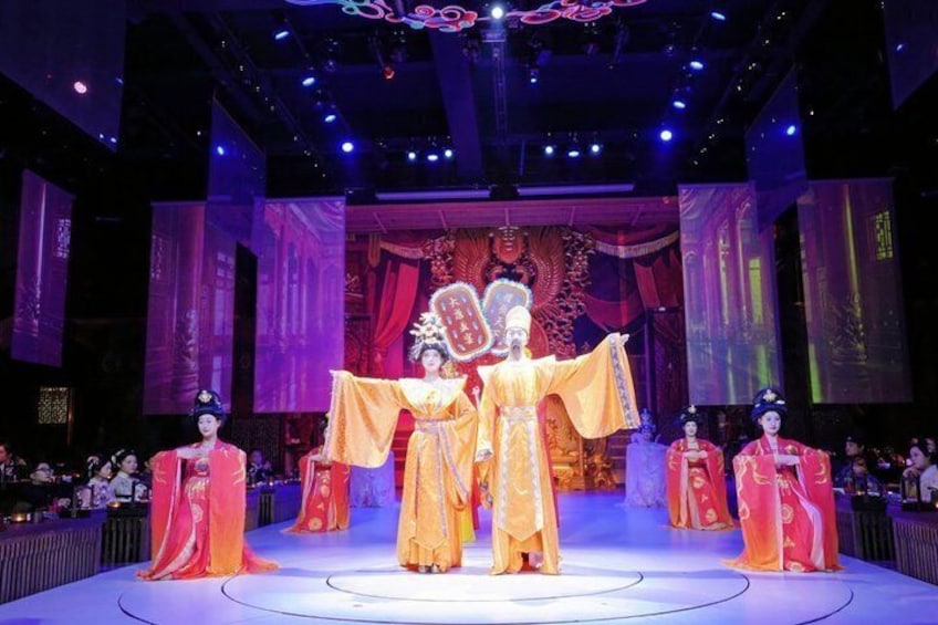 A stage with performers in traditional costumes, a large ornate backdrop, and a seated audience. 3