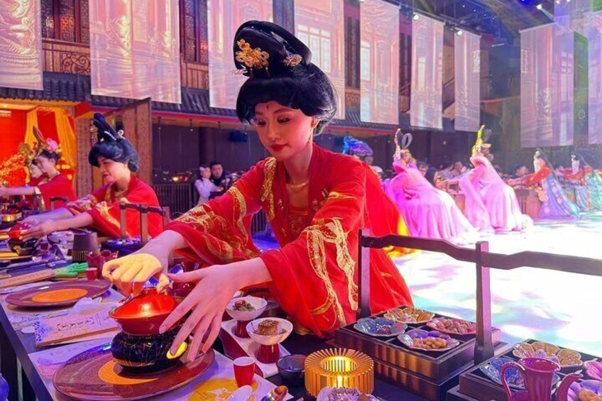 A person in traditional attire serving food at a table with dishes and a teapot. 5