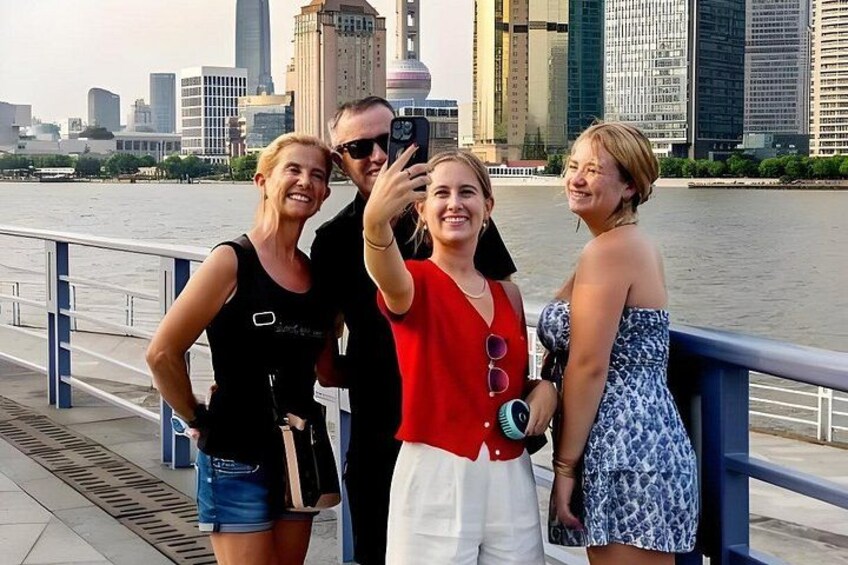 Een groep mensen maakt een selfie aan het water, met een stadsachtergrond op de achtergrond. 2