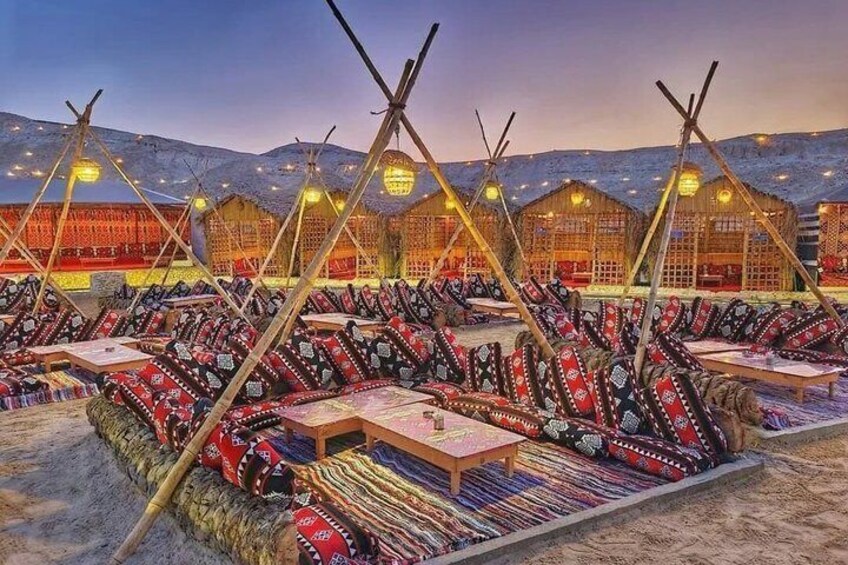 A series of traditional tents with wooden frames and colorful fabric, arranged in rows on a snowy landscape with illuminated buildings in the background. 5
