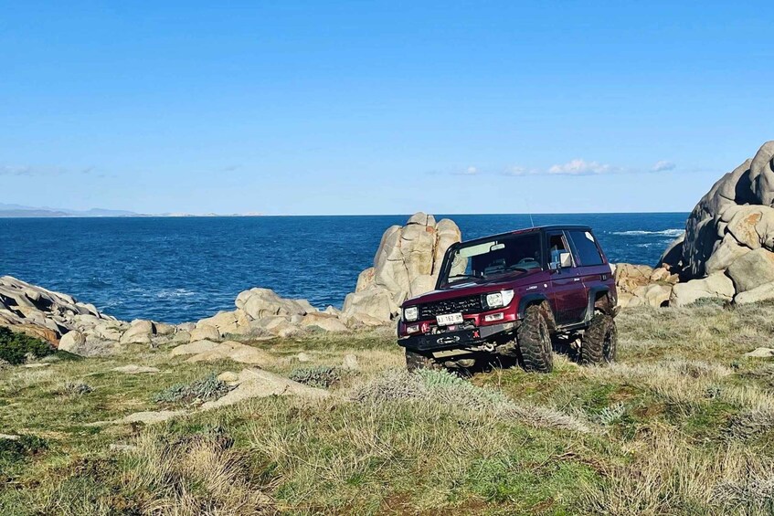 A red SUV parked on rocky terrain near a body of water. 4