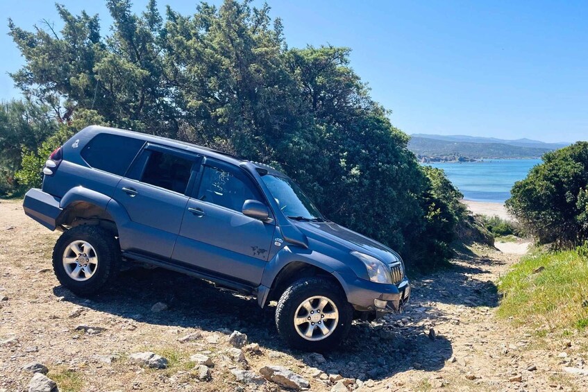 A blue SUV parked on a rocky path with a beach and ocean in the background. 2