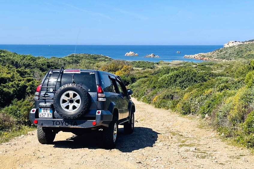 A black SUV on a dirt path with a coastal landscape in the background. 3