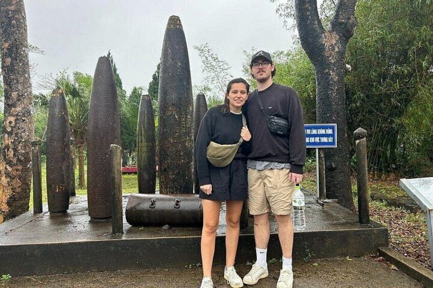 Two people standing in front of tall, pointed structures with a sign in the background. 1