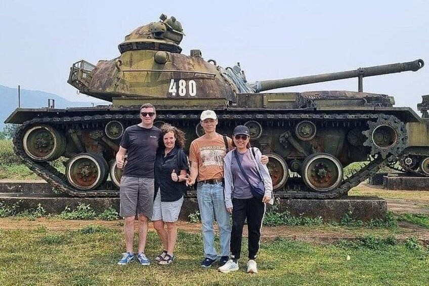 A group of people standing in front of a military tank with the number 480. 2
