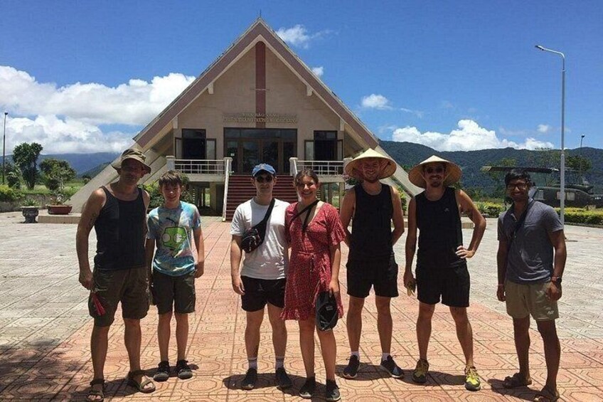 A group of people standing in front of a building with a triangular roof and a staircase leading up to it. 5