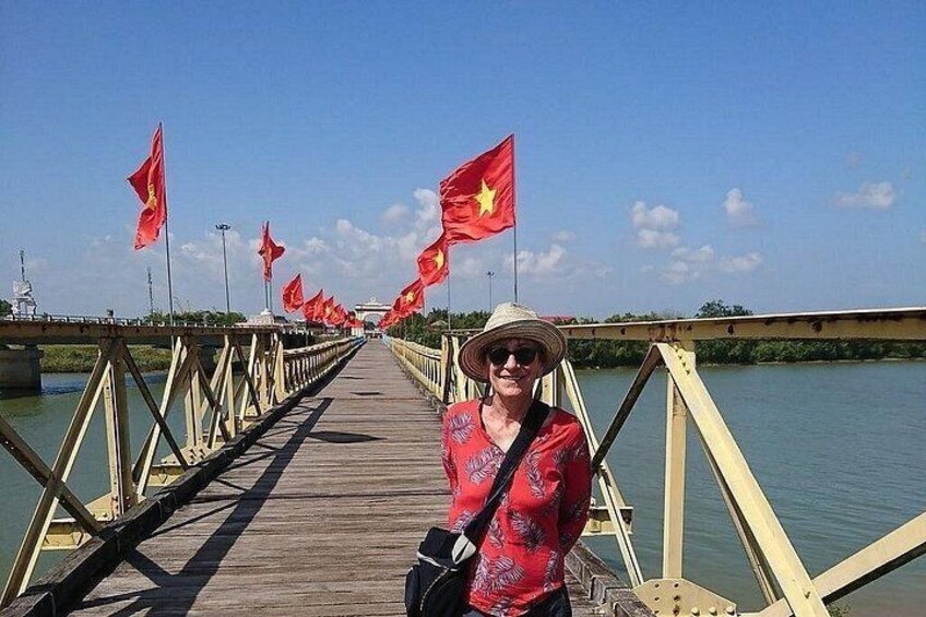 A person standing on a wooden bridge with red flags, overlooking a body of water. 3