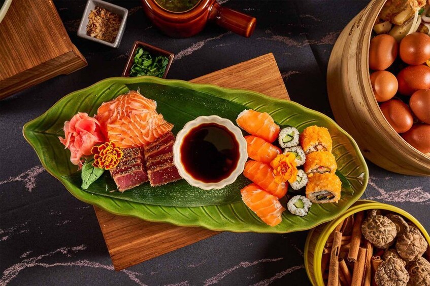 Erilaisia sushilajikkeita tarjoillaan vihreällä lehtitarjottimella, ja joukossa on sekä nigiri- että makirullia. Lisäksi tarjolla on pieni kulho soijakastiketta. 2