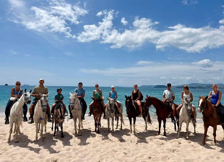 A group of people on horses on a beach with the sea and islands in the background. 3