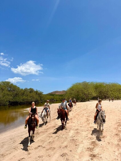 A group of people horseback riding along a riverbank. 1